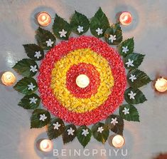 a circular arrangement of flowers and candles on a table with the center surrounded by leaves