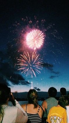 people are watching fireworks in the sky at night with their backs turned to the camera