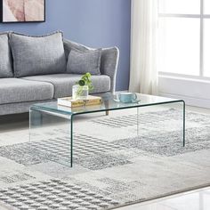 a glass coffee table sitting on top of a rug in front of a gray couch