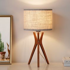 a lamp on a table next to a potted plant and a framed photograph in the corner