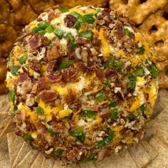 a cheese ball with bacon, green peppers and other toppings on it next to some pretzels