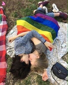 two children laying on a blanket in the grass with a rainbow colored blanket over them