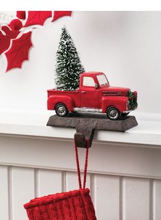 a red truck with christmas tree on top is sitting on a shelf in front of a white wall