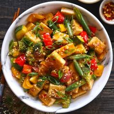 a white bowl filled with tofu and veggies on top of a wooden table