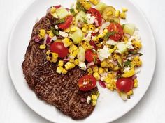 a white plate topped with steak, corn and tomatoes