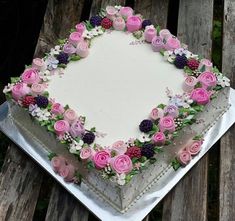 a square cake decorated with pink and purple flowers on top of a wooden table in front of a bench