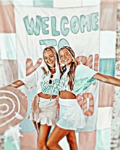 two young women standing next to each other in front of a welcome sign and banner