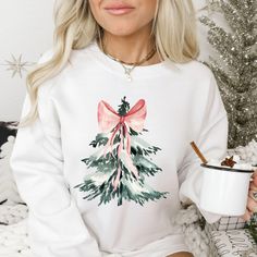 a blonde woman wearing a white sweatshirt with a pink bow and green christmas tree on it