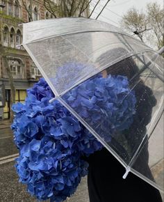 a woman holding an umbrella with blue flowers on it in front of a building and trees