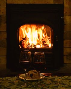 two glasses of wine sitting on a table in front of a fire place that is lit