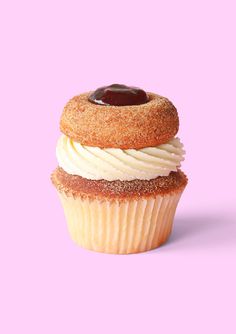 a cupcake with white frosting and a chocolate topping on top, against a pink background