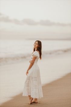 a woman in a white dress standing on the beach