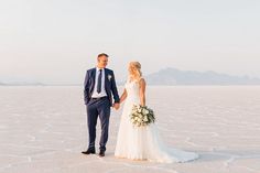 a bride and groom holding hands in the middle of an empty salt flat with mountains in the background