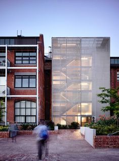 people walking in front of a building that has glass walls on the side and stairs leading up to it