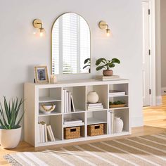 a white shelf with books and plants on it next to a round mirror in the corner