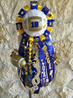 a football themed wine glass with gold and blue ribbon around the neck, on a stone wall