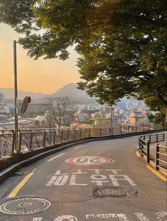 an empty street with graffiti painted on the road and buildings in the background at sunset