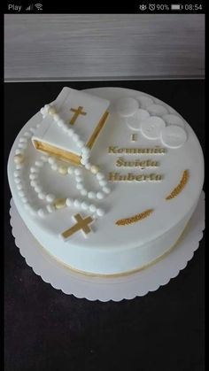 a cake with white frosting and gold decorations on it, including a cross, rosary, and beads