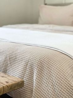 a wooden bench sitting in front of a bed with white sheets and pillows on top of it