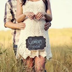 a man and woman standing next to each other holding a sign that says coming soon