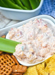 a bowl filled with dip surrounded by crackers and pretzels