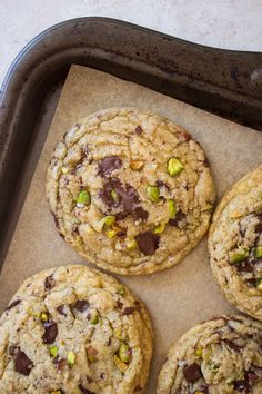 four chocolate chip cookies sitting on top of a baking sheet with pistachios