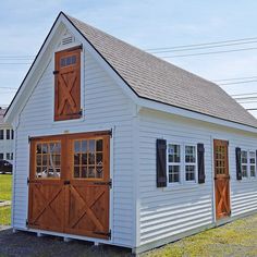 a small white barn with wooden doors and windows