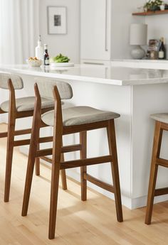 three wooden stools sitting in front of a kitchen island with white counter tops and wood flooring