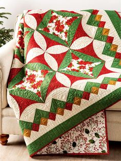 a couch with a christmas quilt on top of it next to a white chair and potted plant