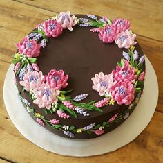 a chocolate cake decorated with pink flowers and green leaves on a white plate sitting on a wooden table