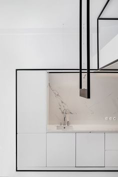 a white kitchen with marble counter tops and cabinets in the center, along with black framed mirrors hanging from the ceiling