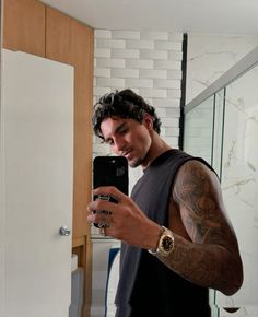 a man with tattoos is looking at his cell phone while standing in front of a mirror