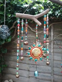 a wind chime hanging from a tree branch in front of a wooden fence with green leaves