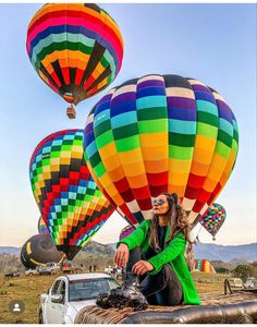 a woman sitting on the back of a truck in front of hot air balloon's