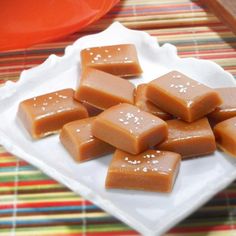 there are many pieces of caramel fudge on the white plate and colorful table cloth