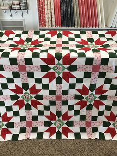 a quilted table cloth with red, green and white designs on it in front of bookshelves