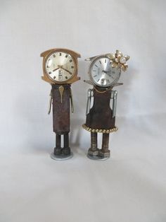 two metal figurines with clocks on their heads, one is wearing a dress