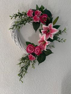 a white wreath with pink flowers and greenery hanging on the side of a wall