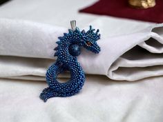 a blue dragon brooch sitting on top of a white cloth next to a red velvet pillow