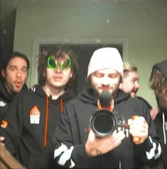 a group of young men standing next to each other wearing black sweatshirts and green goggles