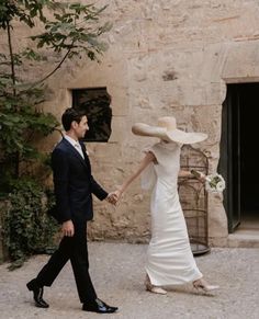 a man and woman holding hands in front of a stone building with a birdcage