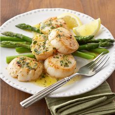 scallops and asparagus are served on a white plate with lemon wedges