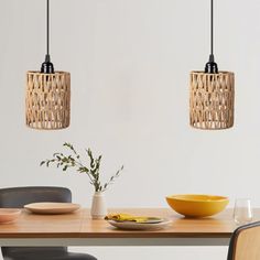 two pendant lights hanging over a wooden table with plates and bowls on the dining room table