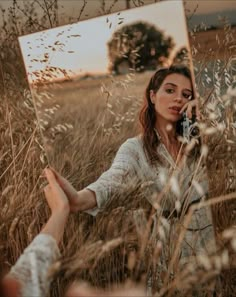 a woman standing in tall grass holding a cell phone to her ear