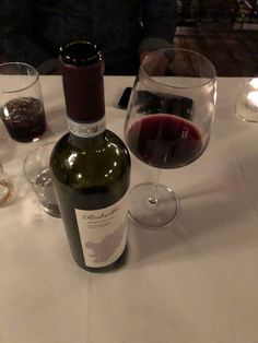 a bottle of wine sitting next to two glasses on a white tablecloth covered table