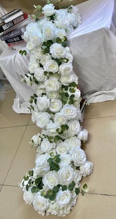 white roses and greenery are arranged in the shape of a vertical column on a tile floor