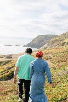 a man and woman walking down a hill near the ocean