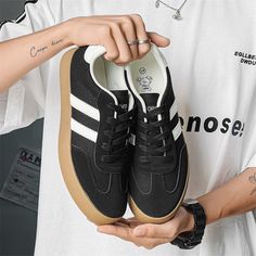 a person holding up a pair of black and white adidas sneakers with brown soles