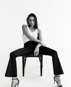 a woman sitting on top of a chair wearing black pants and heels with her legs crossed