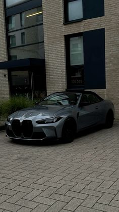 a grey sports car parked in front of a building on a brick sidewalk next to a fire hydrant